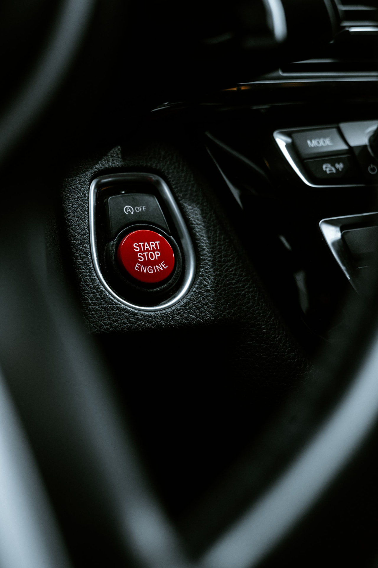 Close-up of a red engine start-stop button on a dark car dashboard